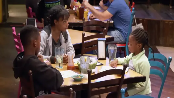 Una madre soltera y sus hijos en un restaurante no se dan cuenta de que hay un hombre sentado detrás de ellas